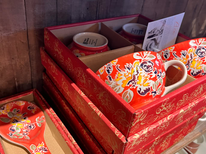 Tasses et cuillères rouges avec motifs floraux jaunes et blancs, présentées dans des boîtes rouges décorées.