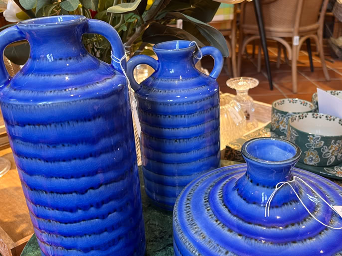 Trois vases bleus en céramique sur une table, entourés d'autres objets décoratifs.