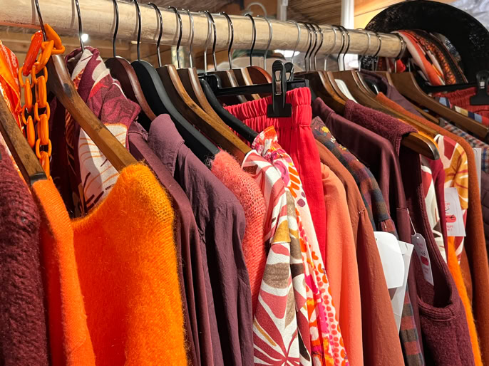 Vêtements suspendus sur des cintres, principalement dans des tons orange et rouge.