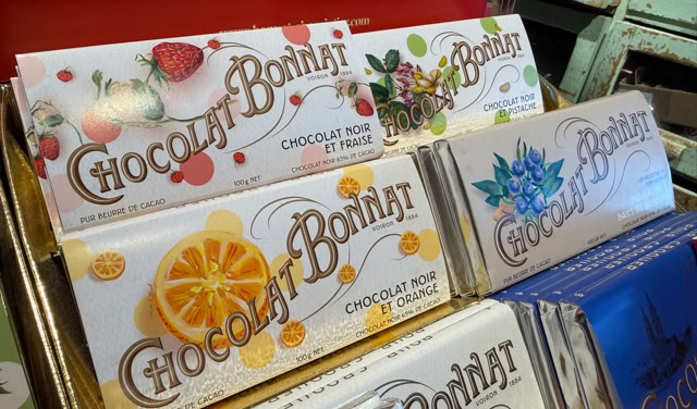 Tablettes de chocolat colorées avec des illustrations de fruits et de fleurs sur les emballages, disposées sur une étagère.