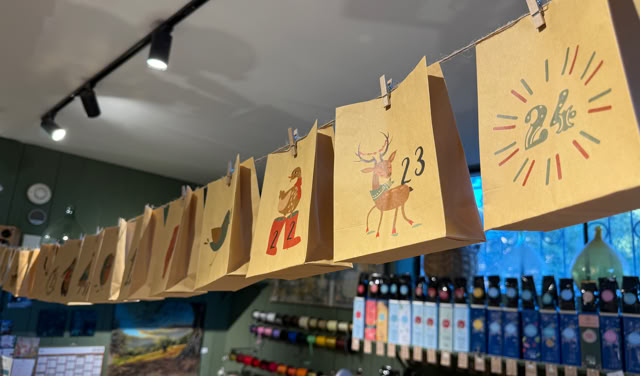 Des sacs en papier numérotés suspendus en ligne, avec des illustrations festives, au-dessus d'étagères de bouteilles dans un magasin.