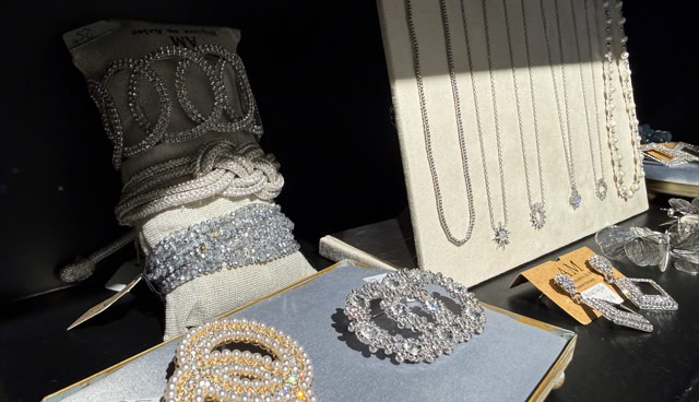 Présentoir de bijoux avec colliers, bracelets et broches en perles et strass, sur fond noir.