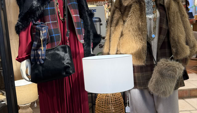 Deux mannequins habillés en vêtements d'hiver, l'un portant une robe rouge et une écharpe, l'autre un manteau en fourrure et un chapeau. Une lampe et une chaise en osier sont placées devant eux.