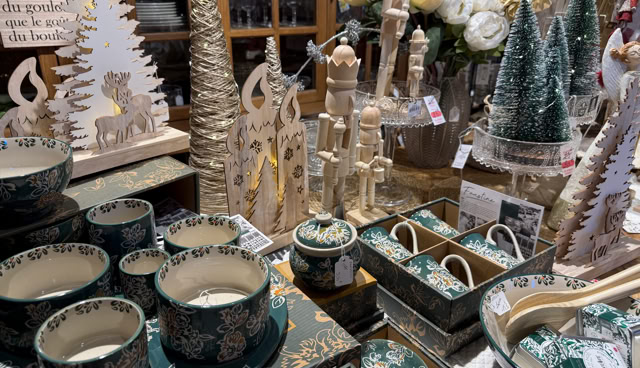 Objets de décoration de Noël sur une table, comprenant des tasses, des assiettes, des sapins miniatures, des figurines en bois et des fleurs.