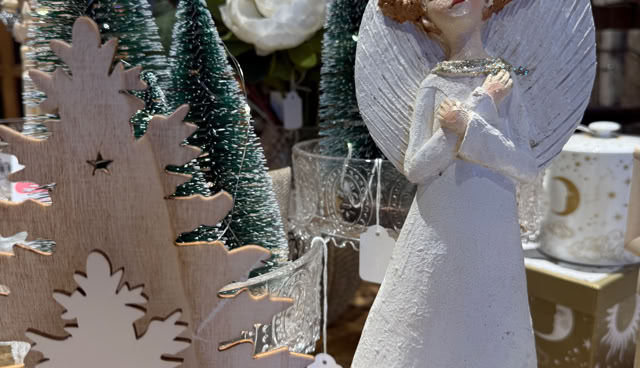 Statue d'ange en céramique blanche avec des ailes, entourée de décorations de Noël, y compris des arbres miniatures et des fleurs blanches.