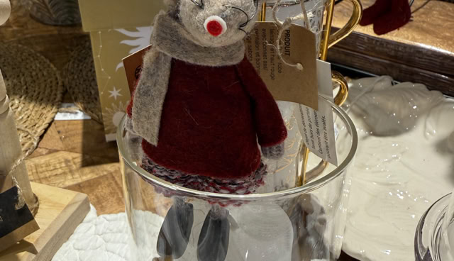 Une peluche de souris en tenue de Noël rouge et blanche, placée dans un vase en verre décoré de feuilles dorées.