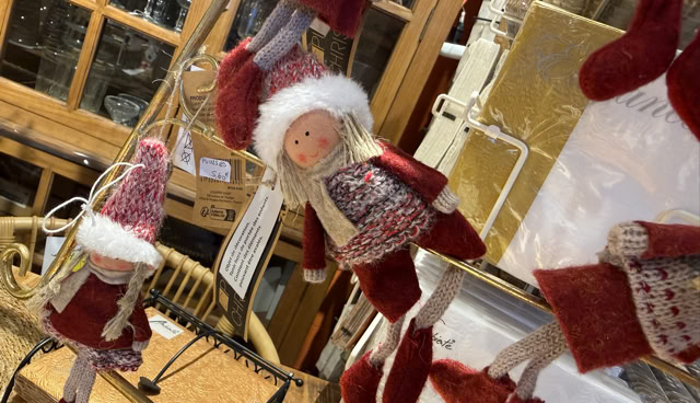 Des décorations de Noël en forme de poupées avec des vêtements rouges et blancs, suspendues dans un magasin.
