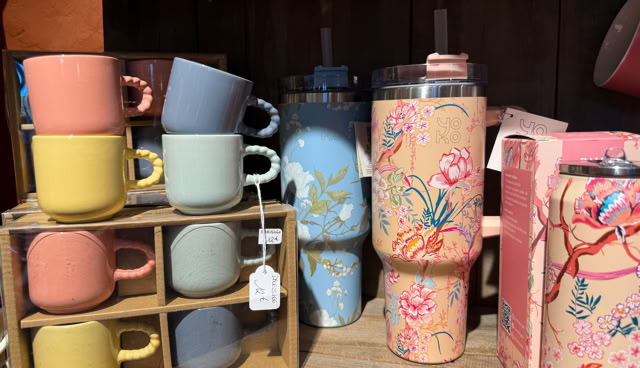 Tasses colorées empilées dans un casier en bois à gauche, et deux grandes bouteilles décorées de motifs floraux à droite.