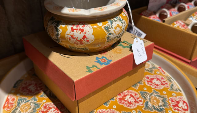 Bol en céramique décoré de motifs floraux jaunes et rouges, posé sur une boîte en carton rouge et beige, avec une étiquette attachée.