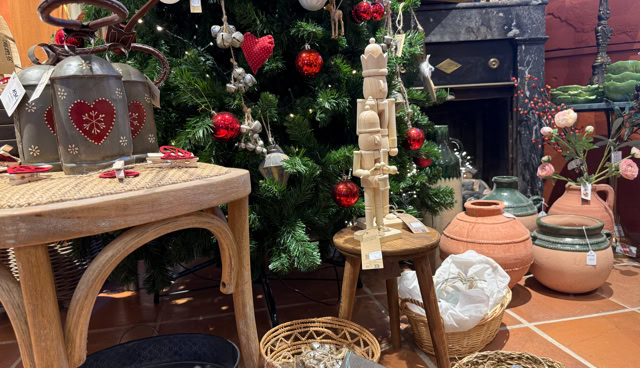 Décoration de Noël avec un sapin orné de boules rouges et blanches, une table en bois avec des objets décoratifs, des paniers contenant divers articles, et des pots en terre cuite.