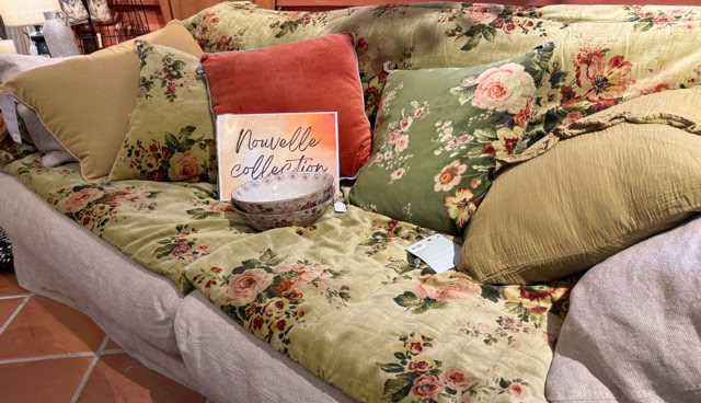 Canapé avec des coussins à motifs floraux et un coussin orange, sur un sol en carreaux de terre cuite.