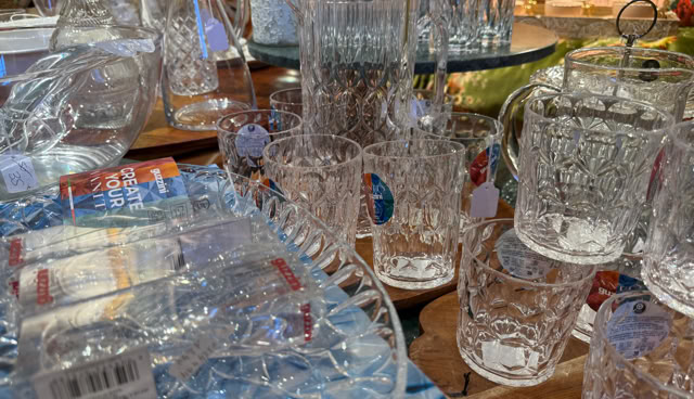 Divers articles en verre, y compris des tasses et des pichets, sont disposés sur une table en bois.
