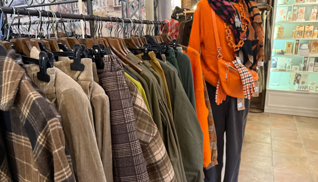 Vêtements suspendus sur des cintres, y compris des vestes à carreaux et des manteaux de différentes couleurs, avec un mannequin portant une écharpe orange et un sac à main.