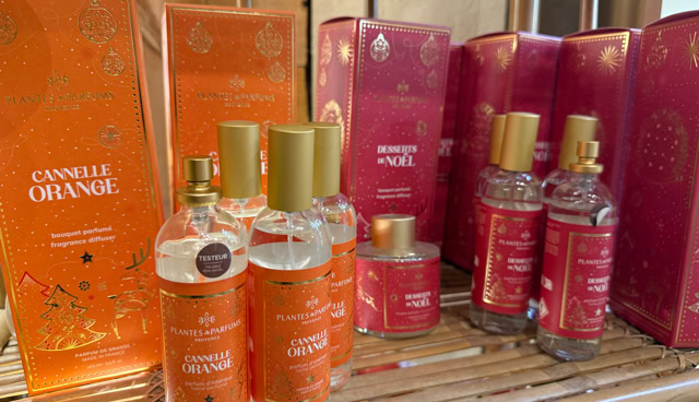 Des boîtes et bouteilles de parfum aux couleurs orange et rose, posées sur une étagère en bois.