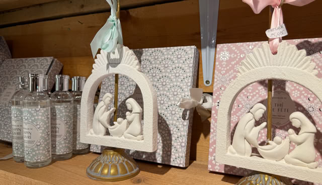 Décorations en céramique représentant une scène de la Nativité sur une étagère en bois, avec des bouteilles en verre à côté.