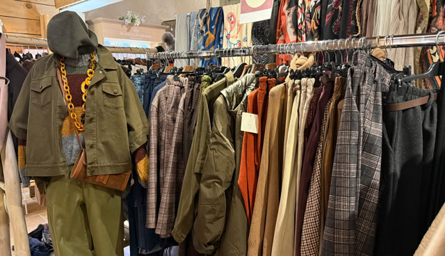 Portant de vêtements avec divers manteaux, chemises et pantalons suspendus, et un mannequin habillé en tenue verte avec un collier.