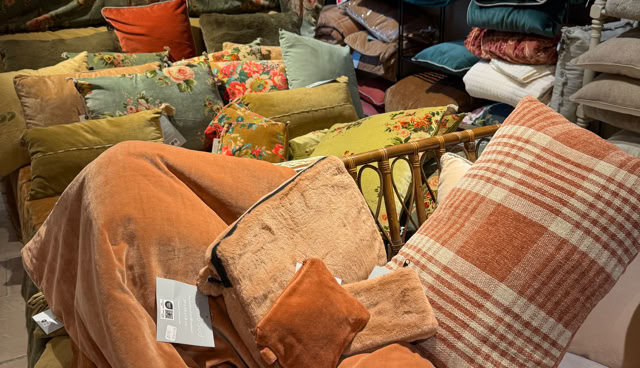 Coussins et couvertures colorés empilés dans un magasin, avec des tons orange, vert et bleu.