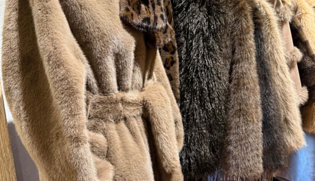 Manteaux en fourrure suspendus sur un portant, avec un foulard à motifs léopard sur l'un d'eux, sol en carreaux de terre cuite.