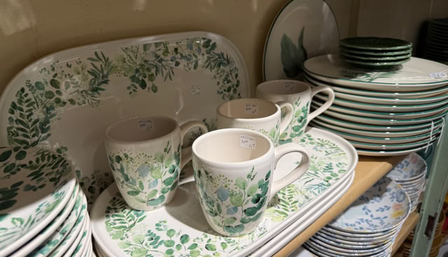 Assiettes, tasses et plateaux avec motifs verts et floraux empilés sur une étagère.