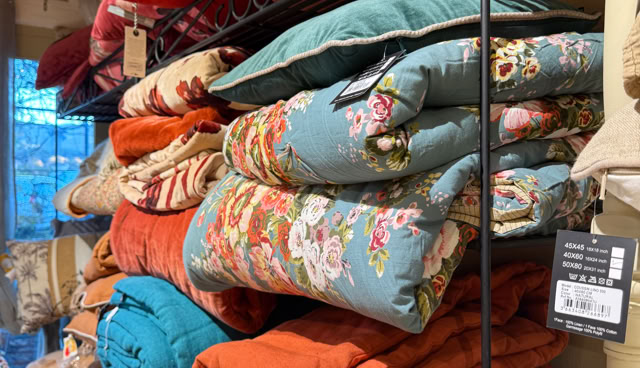 Étagère avec des couvertures et des coussins colorés empilés, comprenant des motifs floraux et des couleurs unies comme le rouge, le bleu et l'orange.