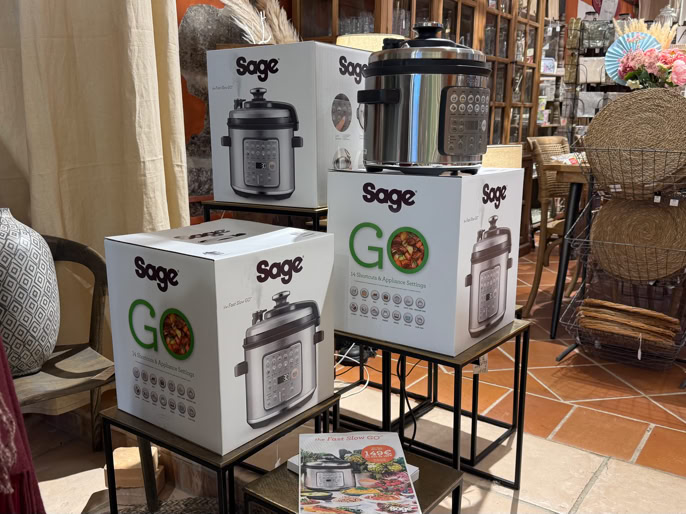Boîtes de cuiseurs exposées sur des étagères dans un magasin, avec des chaises et des tables en arrière-plan.