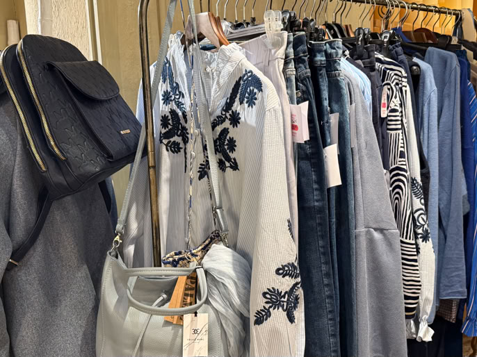 Vêtements suspendus sur un portant, comprenant des vestes, des chemises et un sac à main argenté.