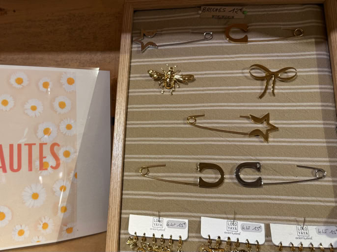 Boîte avec le mot "NOUVEAUTES" à gauche et présentoir de bijoux dorés à droite.