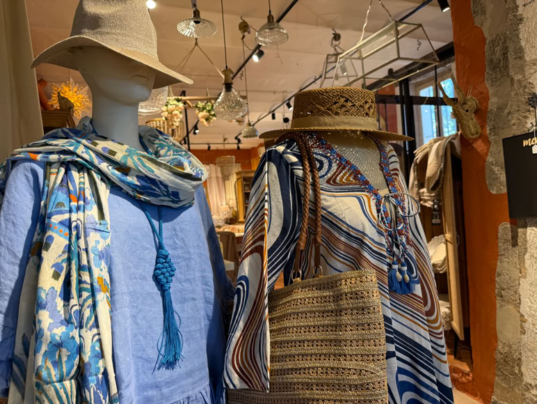 Boutique de vêtements avec des manteaux, vestes et chemises suspendus sur des portants, et des sacs à main exposés.