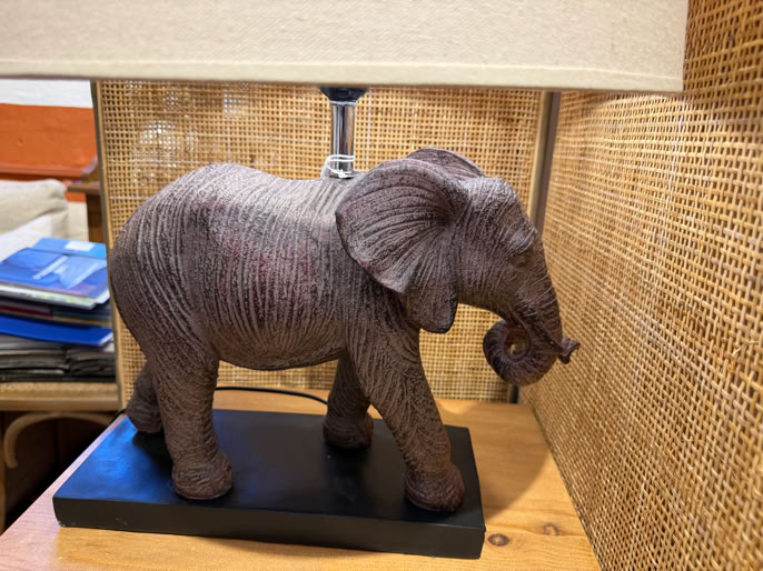 Lampe avec base en forme d'éléphant en bois sur une table, avec un abat-jour beige.