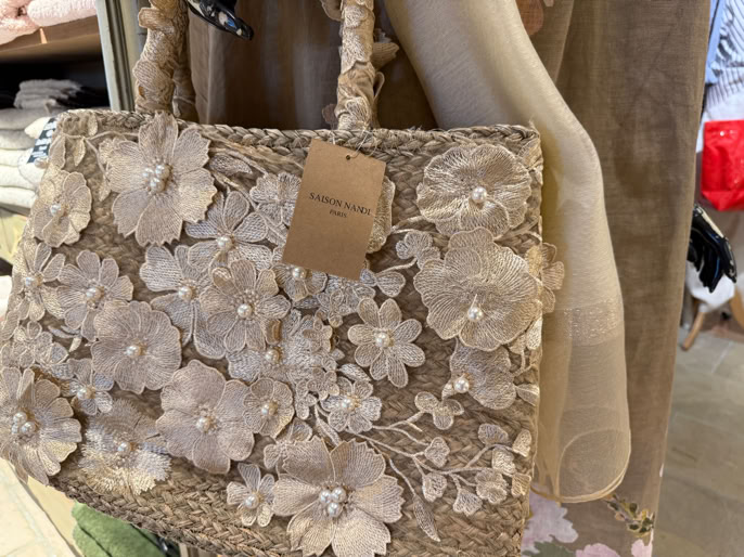 Sac en paille orné de fleurs blanches en relief avec une étiquette attachée, suspendu à un présentoir.