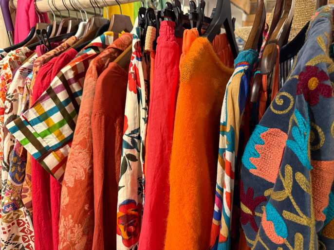 Vêtements colorés suspendus sur des cintres, comprenant des motifs à carreaux, floraux et unis.