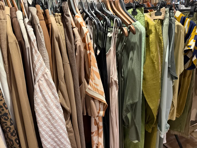 Vêtements suspendus sur des cintres dans une boutique, avec des tons de beige, vert et jaune.