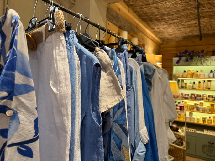 Vêtements bleus et blancs suspendus sur un portant dans une pièce éclairée, avec des étagères en arrière-plan.